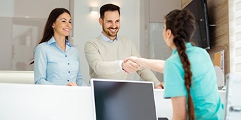 dental assistant shaking male patient’s hand at front desk 