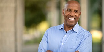 a person smiling with their arms crossed while standing outside