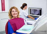 Woman in maroon bib in dental chair smiling