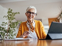Woman in yellow sweater holding pen smiling with tablet