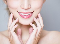 Nose to shoulder view of a woman smiling and touching her jaw