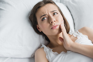 Woman with toothache in bed looking concerned