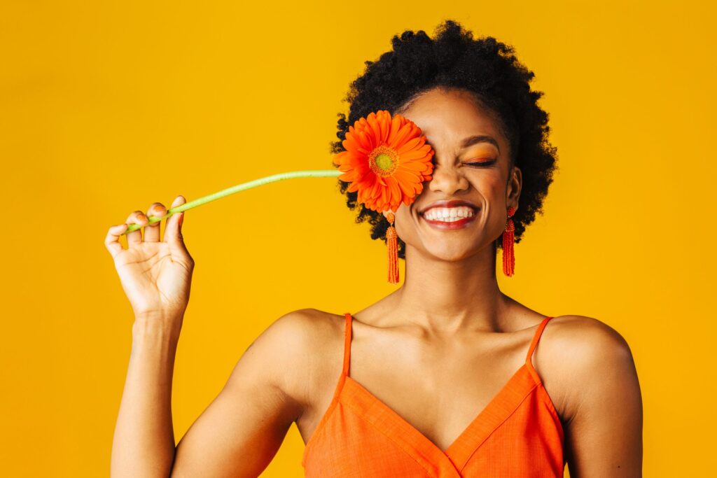 Woman wearing orange holding flower to her smiling face